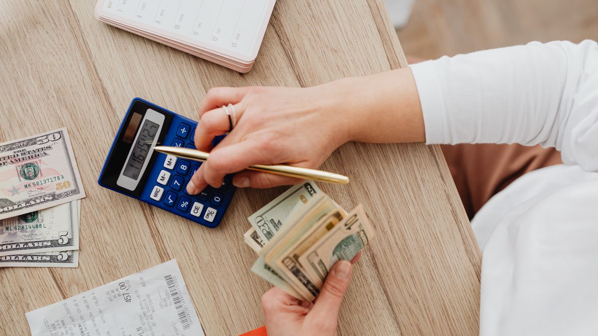 Person using a calculator and counting cash on a wooden table with receipts