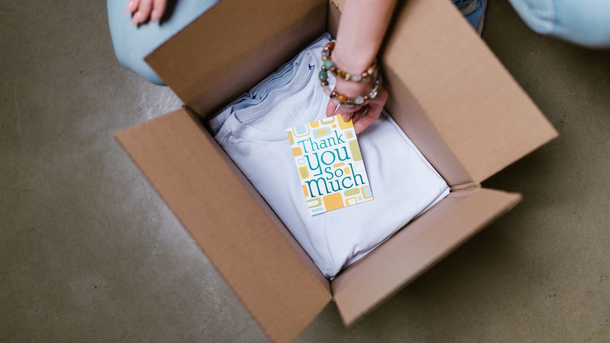 A person packing a white t-shirt with a thank you card into a cardboard box