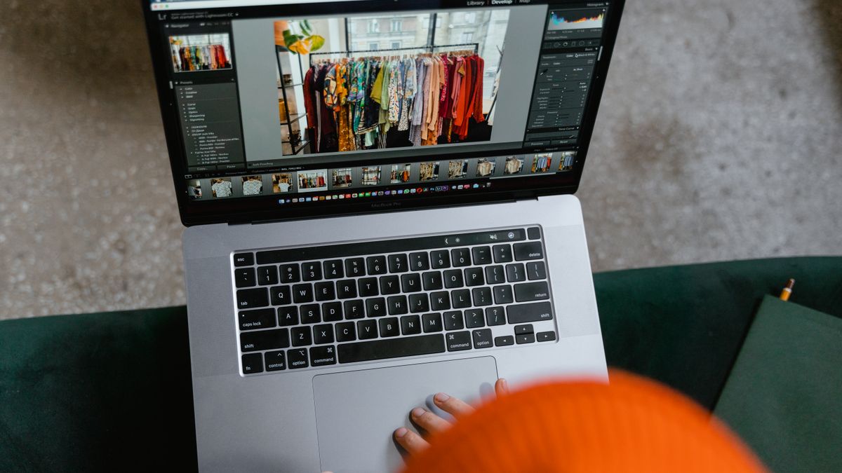 A person in a cozy setting edits photos of clothing displays on a laptop