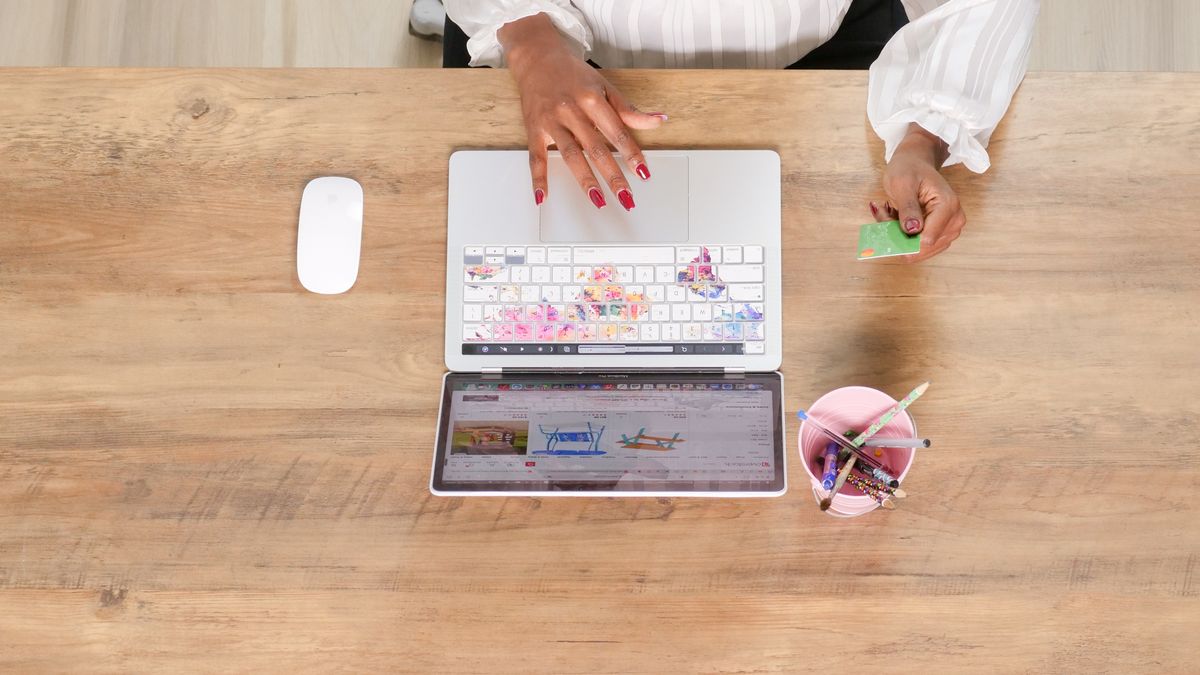 Female hand using a credit card while shopping online on a laptop from a top view angle