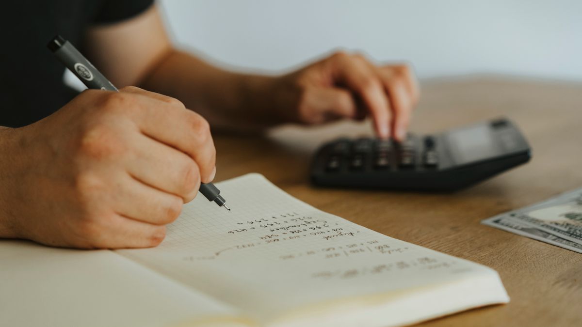 Close-up of hands writing calculations in a notebook with a calculator, focused on budgeting or financial work