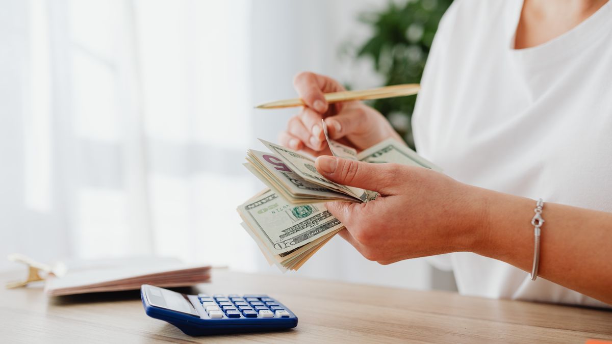 Close-up of a woman holding US dollars, calculating finances at home