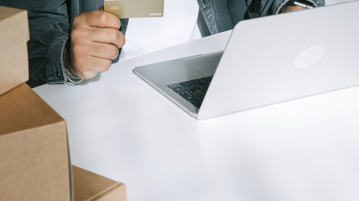 Person using a credit card for online shopping on a laptop surrounded by shipping boxes