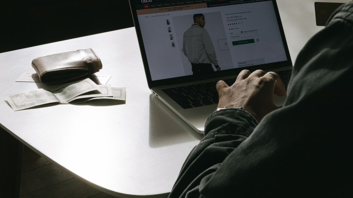 Adult man shopping for clothes online at home using a laptop, with a wallet on the table