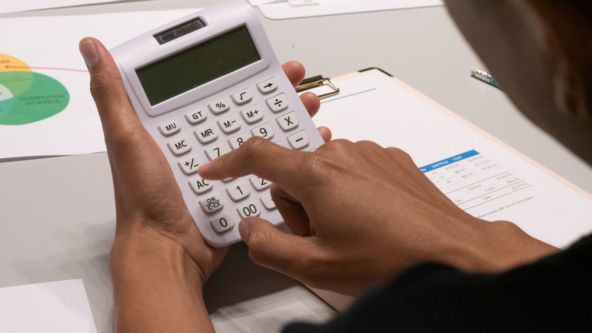 Focused image of a person using a calculator amidst financial documents and charts