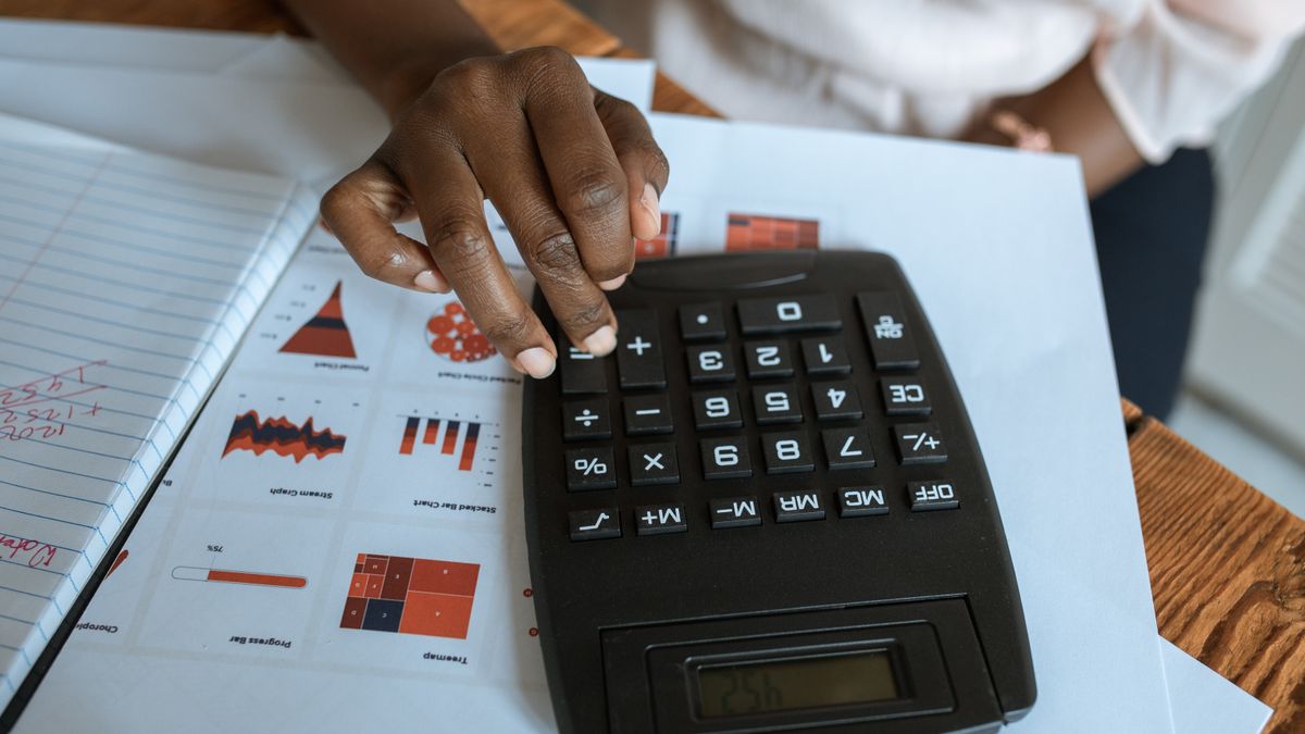 Person using calculator on desk with financial charts and graphs, ideal for business and finance themes