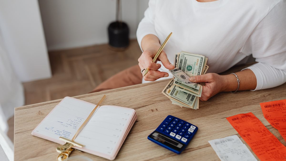 Woman sorting finances with a calculator, cash, and receipts at a desk