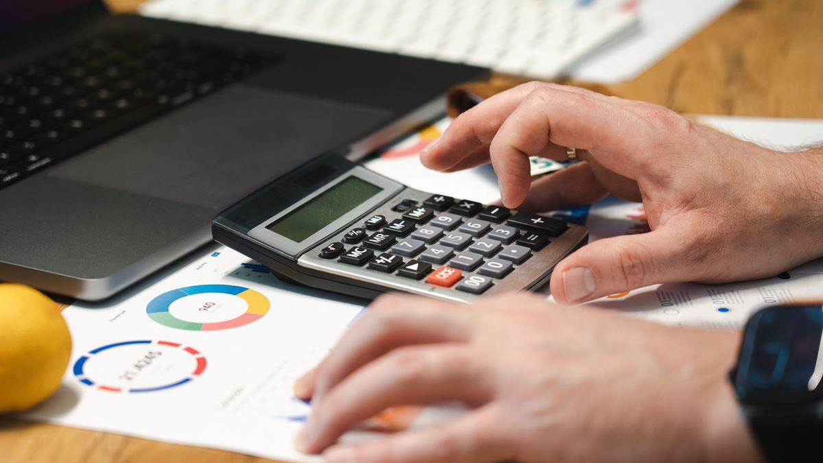 A person analyzing financial data using a calculator and laptop on a desk