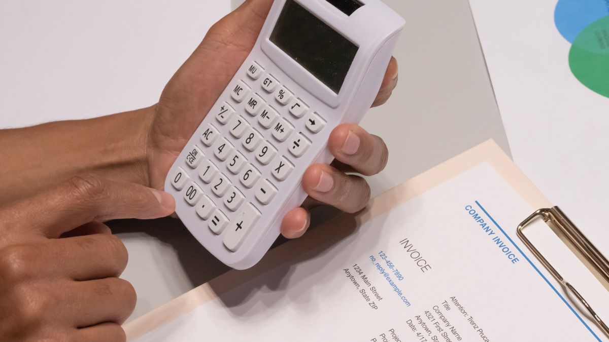 Close-up of hands using a calculator next to a company invoice, depicting a financial calculation concept