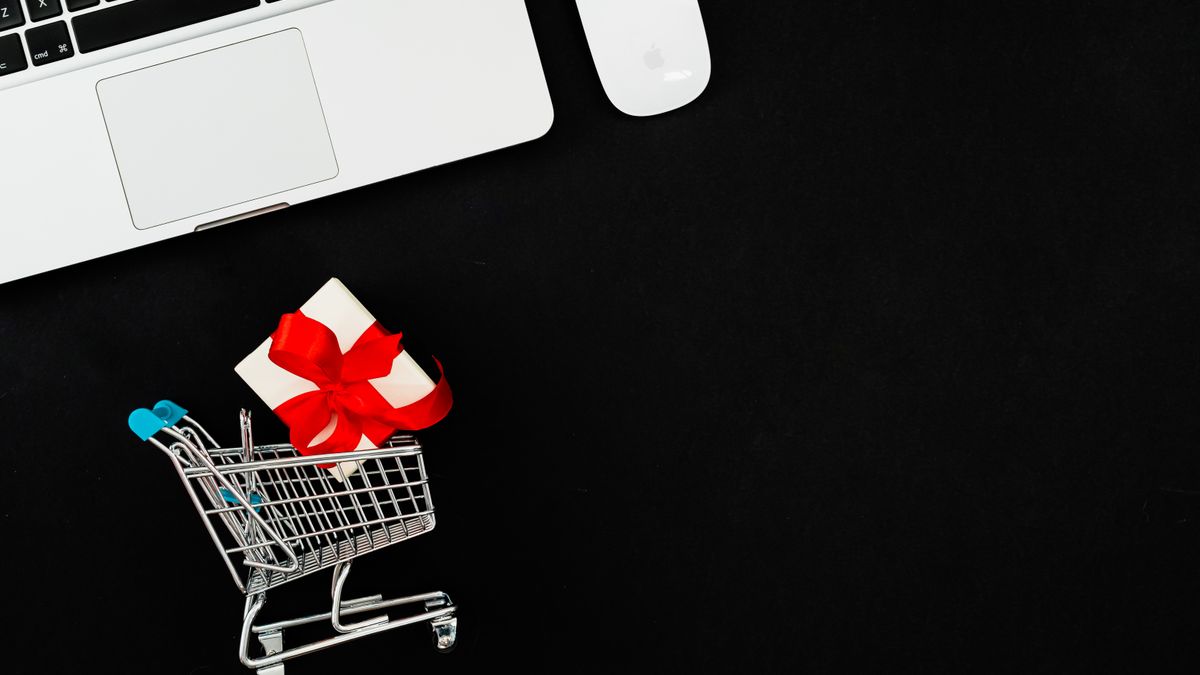Minimalist image of a shopping cart with a gift on a black background beside a laptop, ideal for ecommerce themes