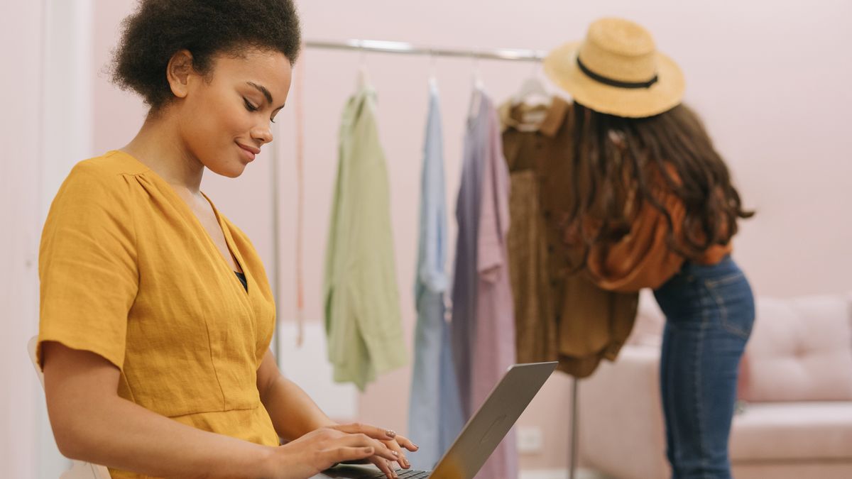 Woman in yellow dress working on laptop in small fashion boutique