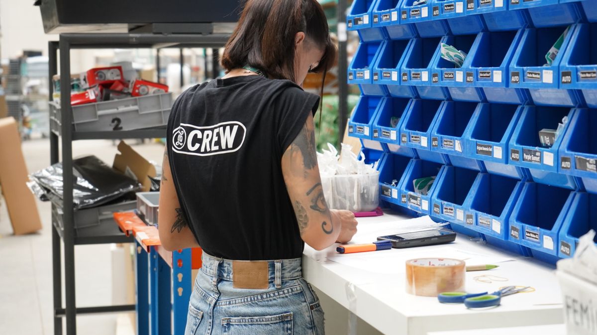 A warehouse worker organizing parts in a storage facility with blue bins and a clipboard