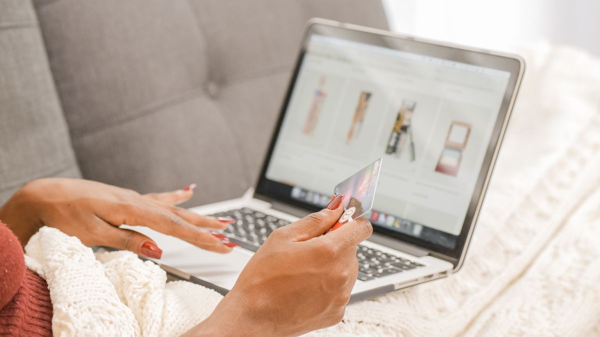 A woman relaxes on a couch while shopping online using her laptop and credit card
