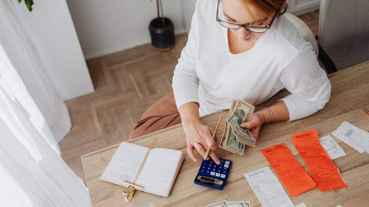 Top view of a woman managing finances with a calculator, cash, and bills in a home setting
