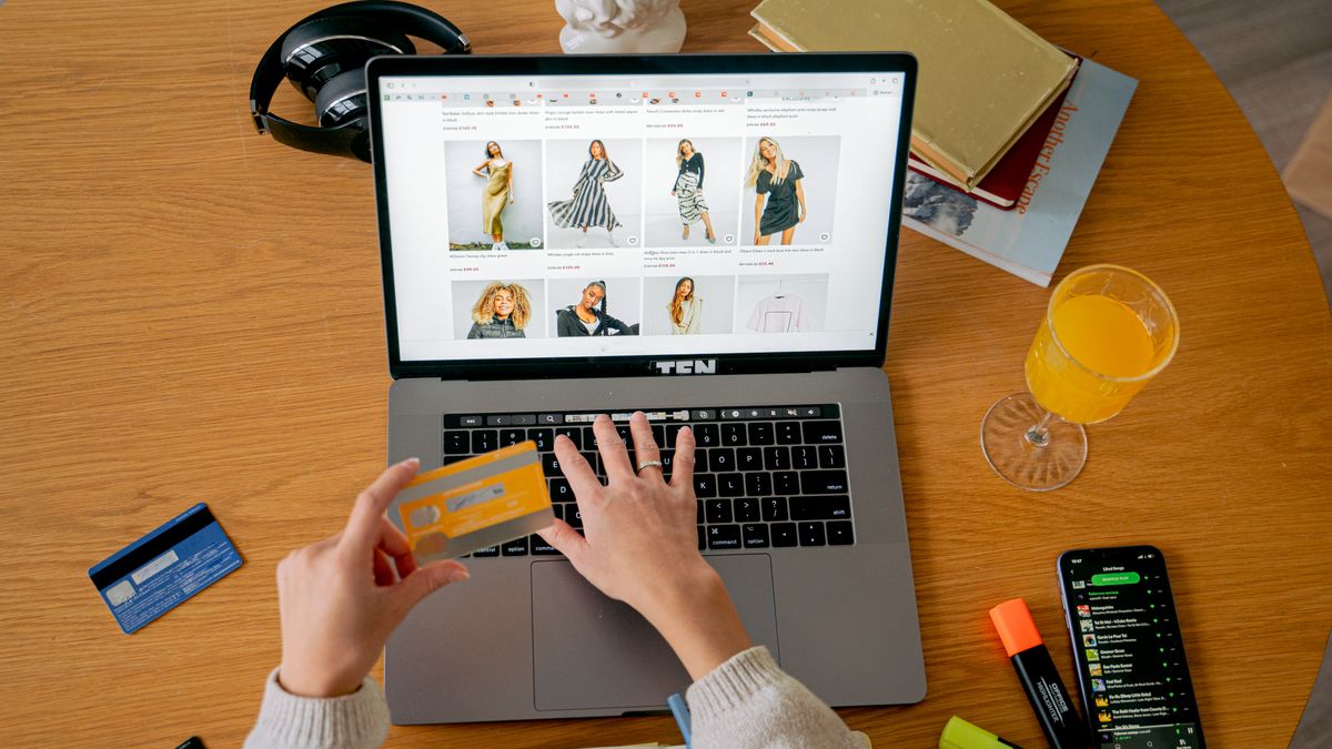 Hands holding credit card making online purchase on laptop at wooden desk with various items